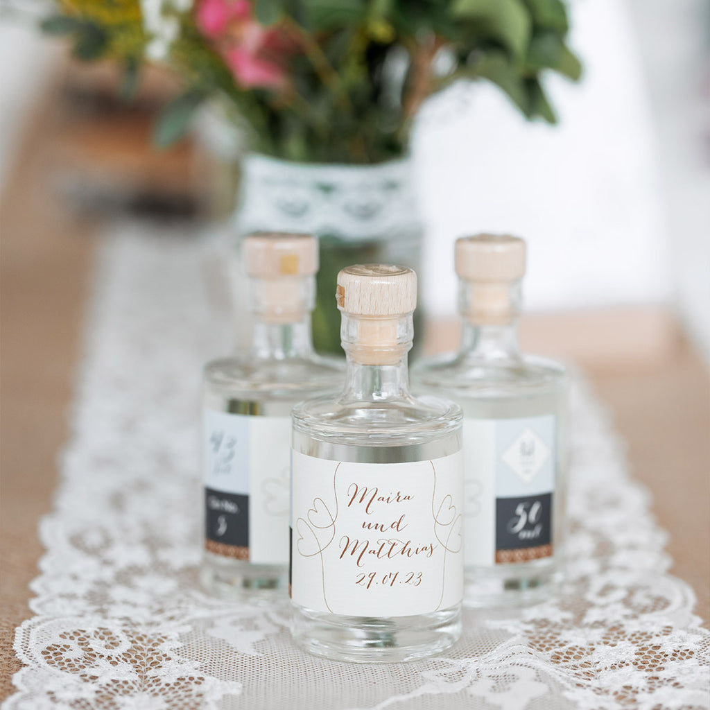 Mit dem Hochzeitskonfigurator von Aromahopping personalisierbare Gin-Flaschen stehen auf einer dekorierten Tafel.