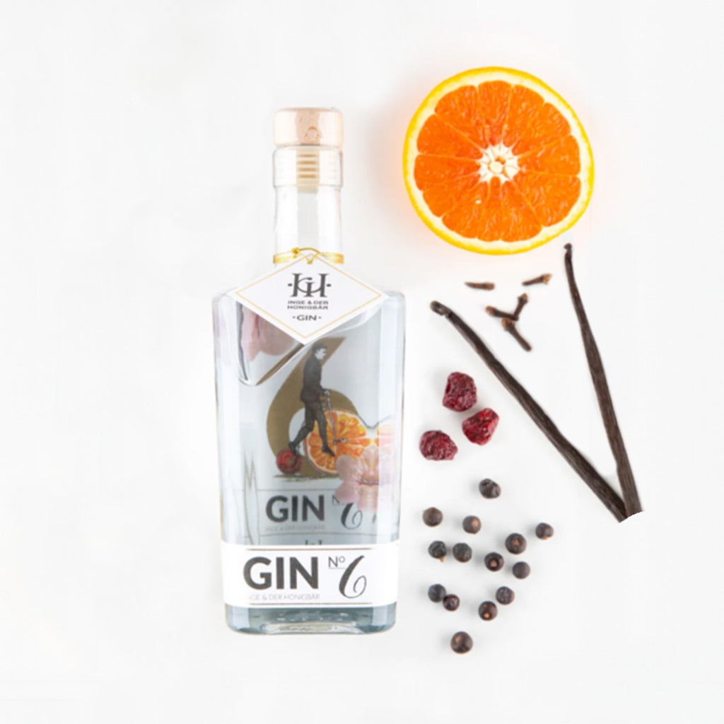 Ingredients liegen neben einer Flasche Premium-Gin NO. 6 Vanille & Kirsche von Inge und der Honigbär, auf weißem Hintergrund.